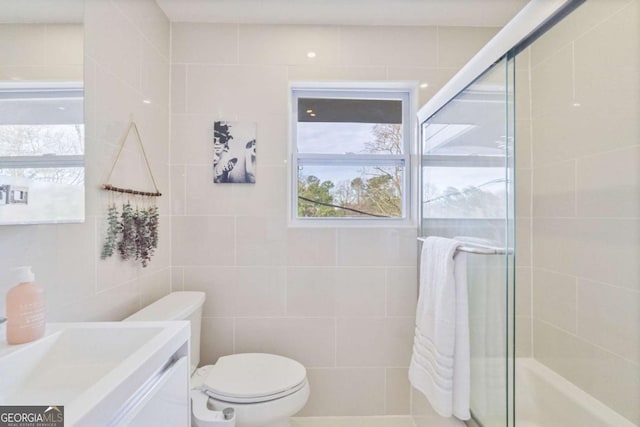 bathroom with vanity, a shower with shower door, tile walls, and toilet