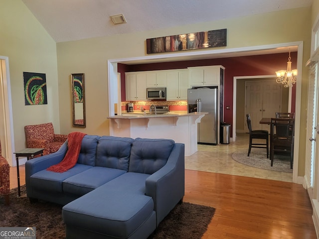 living room with lofted ceiling, a notable chandelier, and light hardwood / wood-style flooring