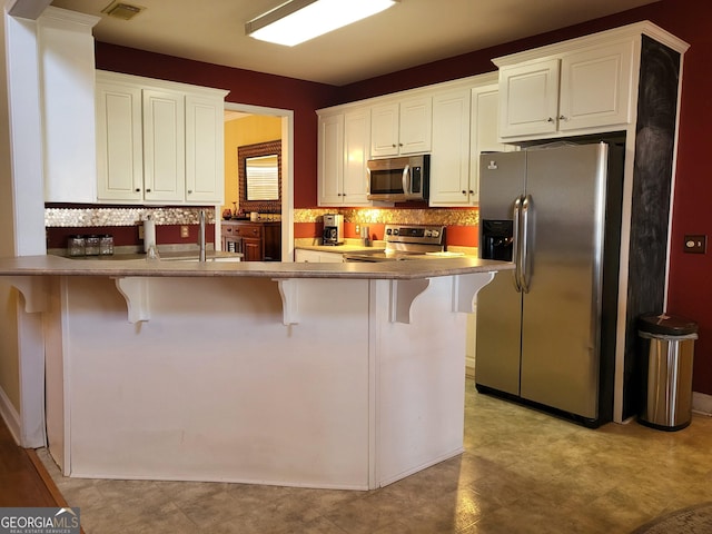 kitchen featuring stainless steel appliances, a breakfast bar, white cabinets, and kitchen peninsula