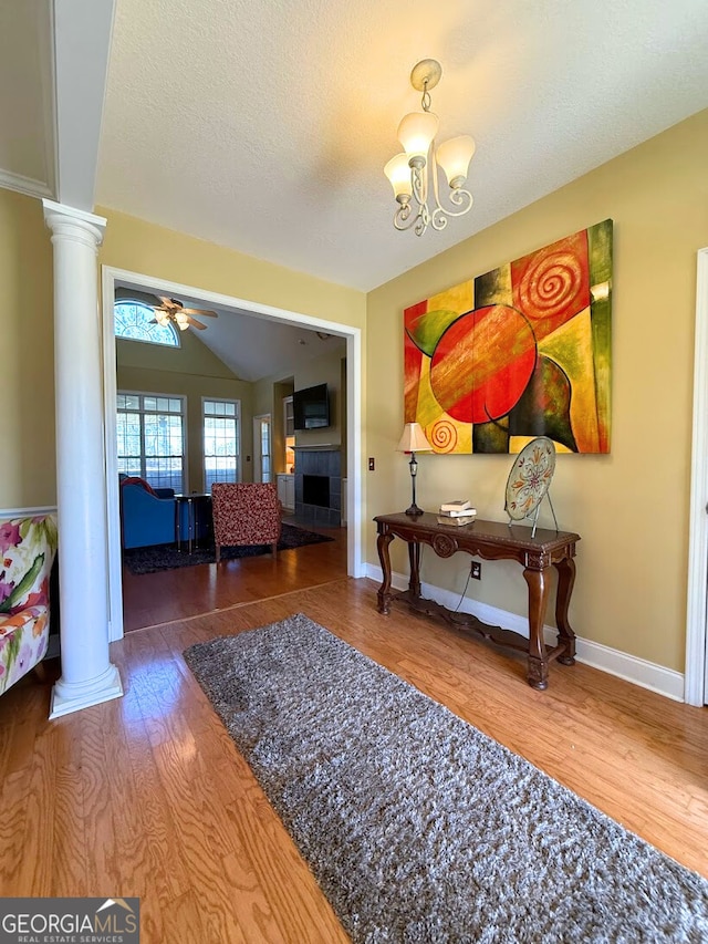 interior space with ceiling fan with notable chandelier, wood finished floors, a fireplace, lofted ceiling, and ornate columns