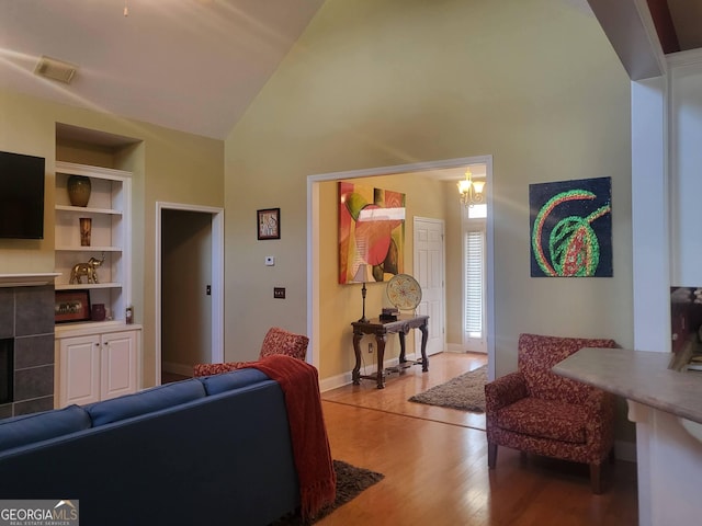 living room featuring built in features, high vaulted ceiling, a fireplace, hardwood / wood-style flooring, and a notable chandelier