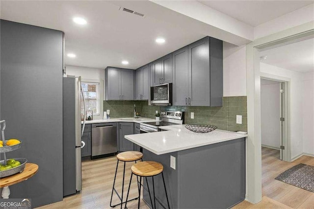 kitchen featuring gray cabinets, appliances with stainless steel finishes, a breakfast bar area, kitchen peninsula, and light wood-type flooring