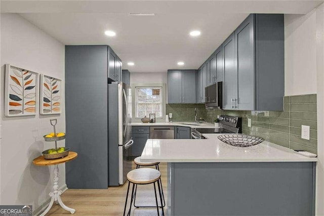 kitchen with a kitchen bar, sink, appliances with stainless steel finishes, kitchen peninsula, and light hardwood / wood-style floors