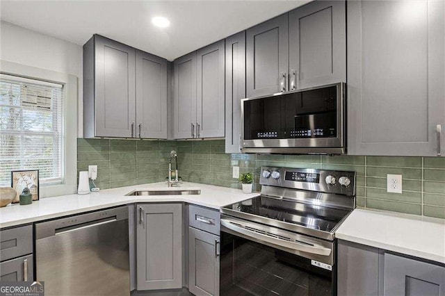 kitchen with tasteful backsplash, appliances with stainless steel finishes, gray cabinets, and sink