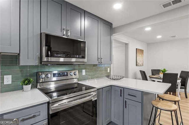 kitchen featuring gray cabinetry, a breakfast bar area, stainless steel appliances, and kitchen peninsula