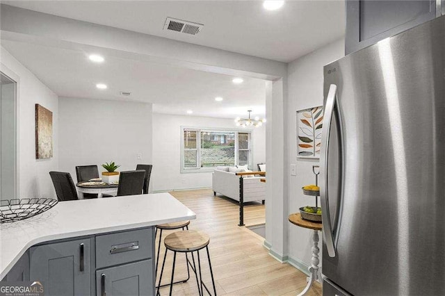 kitchen featuring stainless steel refrigerator, light wood-type flooring, gray cabinetry, a breakfast bar area, and an inviting chandelier