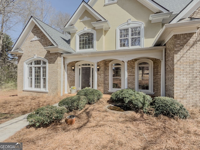 exterior space featuring brick siding, roof with shingles, and stucco siding