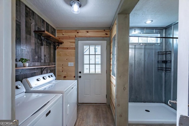 clothes washing area with washer and clothes dryer, wooden walls, a textured ceiling, and light hardwood / wood-style flooring