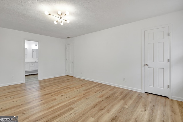 unfurnished bedroom with ensuite bathroom, an inviting chandelier, a textured ceiling, and light hardwood / wood-style floors