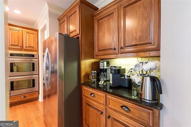 kitchen with appliances with stainless steel finishes, backsplash, dark stone counters, ornamental molding, and light hardwood / wood-style floors