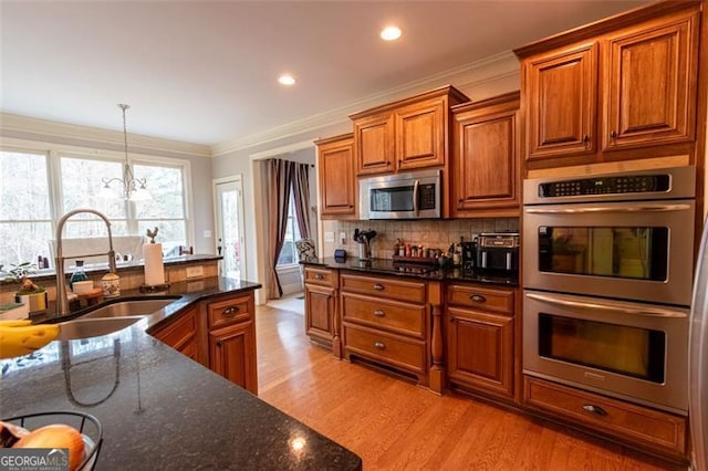 kitchen with decorative light fixtures, sink, dark stone countertops, light hardwood / wood-style floors, and stainless steel appliances