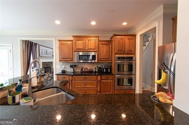 kitchen with appliances with stainless steel finishes, a fireplace, sink, and dark stone counters