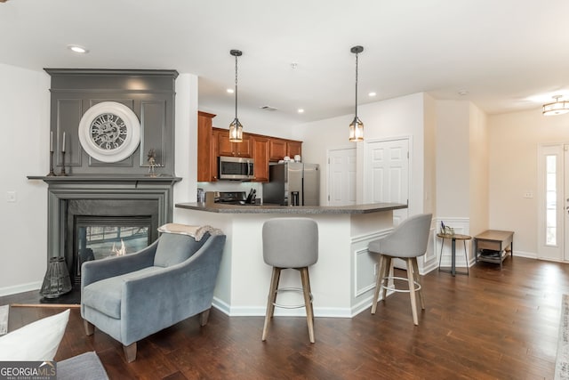 kitchen featuring a kitchen bar, appliances with stainless steel finishes, dark hardwood / wood-style floors, pendant lighting, and a fireplace