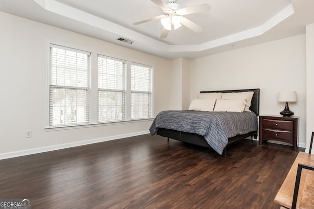 bedroom with dark hardwood / wood-style flooring, a tray ceiling, and ceiling fan