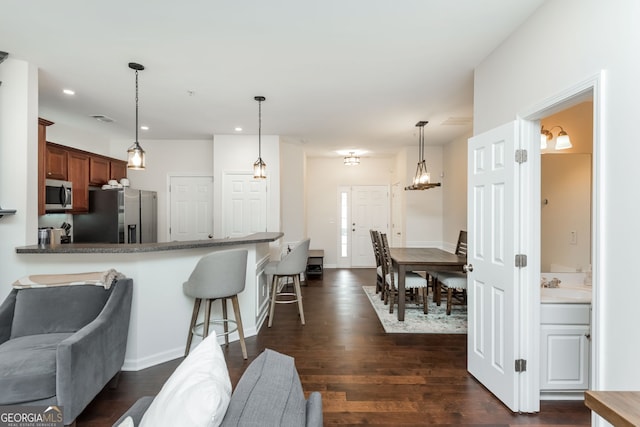 kitchen with a breakfast bar, decorative light fixtures, dark hardwood / wood-style floors, kitchen peninsula, and stainless steel appliances