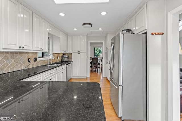 kitchen featuring appliances with stainless steel finishes, sink, white cabinets, dark stone counters, and light wood-type flooring