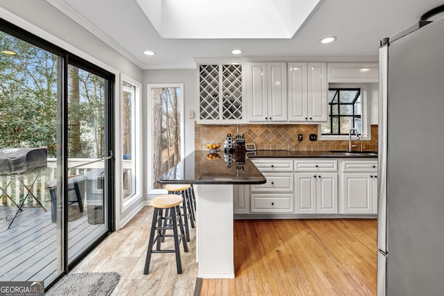 kitchen with sink, stainless steel fridge, a kitchen breakfast bar, white cabinets, and kitchen peninsula