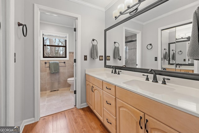 bathroom featuring tile walls, hardwood / wood-style flooring, vanity, toilet, and crown molding