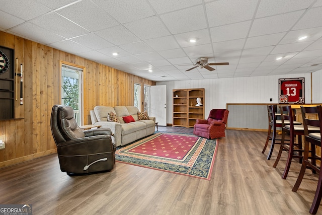 living room with hardwood / wood-style flooring, ceiling fan, bar area, and wooden walls