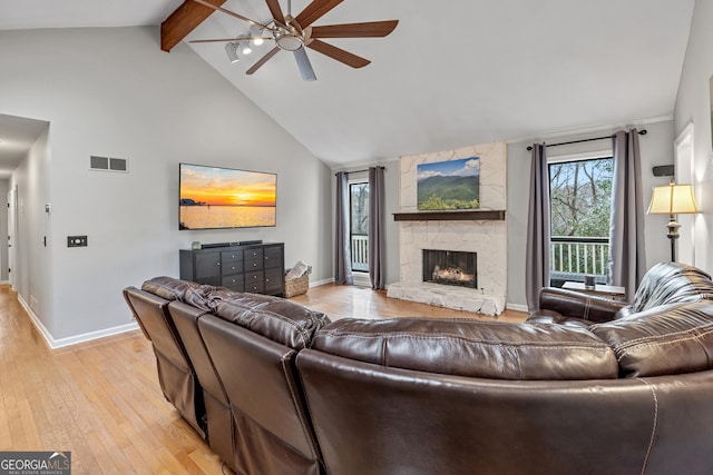 living room featuring a stone fireplace, high vaulted ceiling, light wood-type flooring, beamed ceiling, and ceiling fan