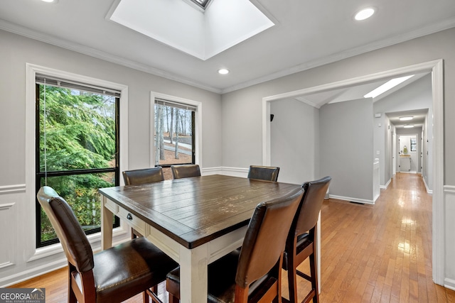 dining area with crown molding, a skylight, and light hardwood / wood-style floors