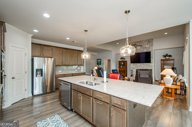 kitchen featuring pendant lighting, sink, backsplash, a kitchen island with sink, and stainless steel appliances