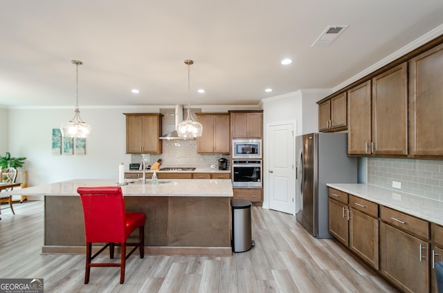 kitchen featuring appliances with stainless steel finishes, sink, hanging light fixtures, a kitchen island with sink, and wall chimney range hood