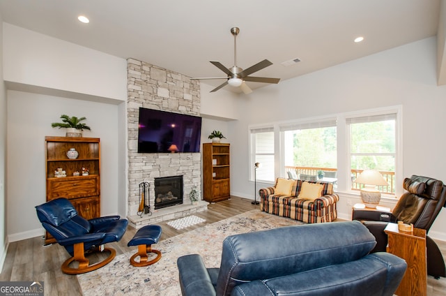 living room featuring a stone fireplace, light hardwood / wood-style flooring, and ceiling fan