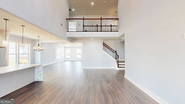 unfurnished living room with a notable chandelier, stairway, dark wood-type flooring, and baseboards