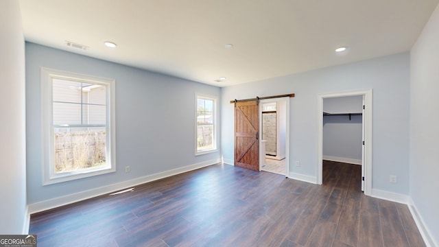 unfurnished bedroom featuring a barn door, baseboards, dark wood finished floors, and a spacious closet
