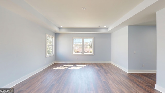 spare room with recessed lighting, a tray ceiling, baseboards, and dark wood-style flooring