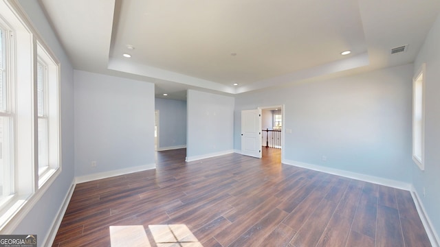 empty room featuring a tray ceiling, visible vents, and dark wood-style flooring