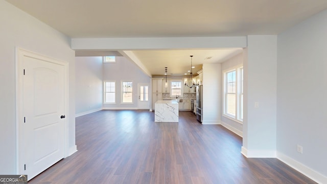 unfurnished living room featuring plenty of natural light, dark wood-style floors, baseboards, and a chandelier