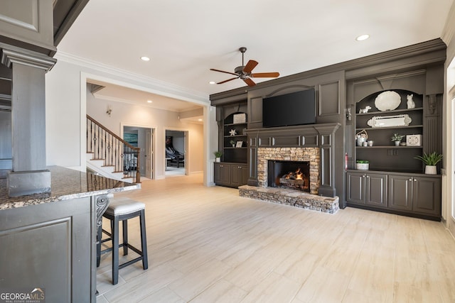 living room featuring built in shelves, decorative columns, light wood-type flooring, ceiling fan, and a fireplace