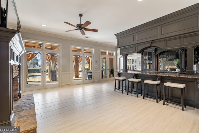 bar with ceiling fan, ornamental molding, french doors, and dark stone counters