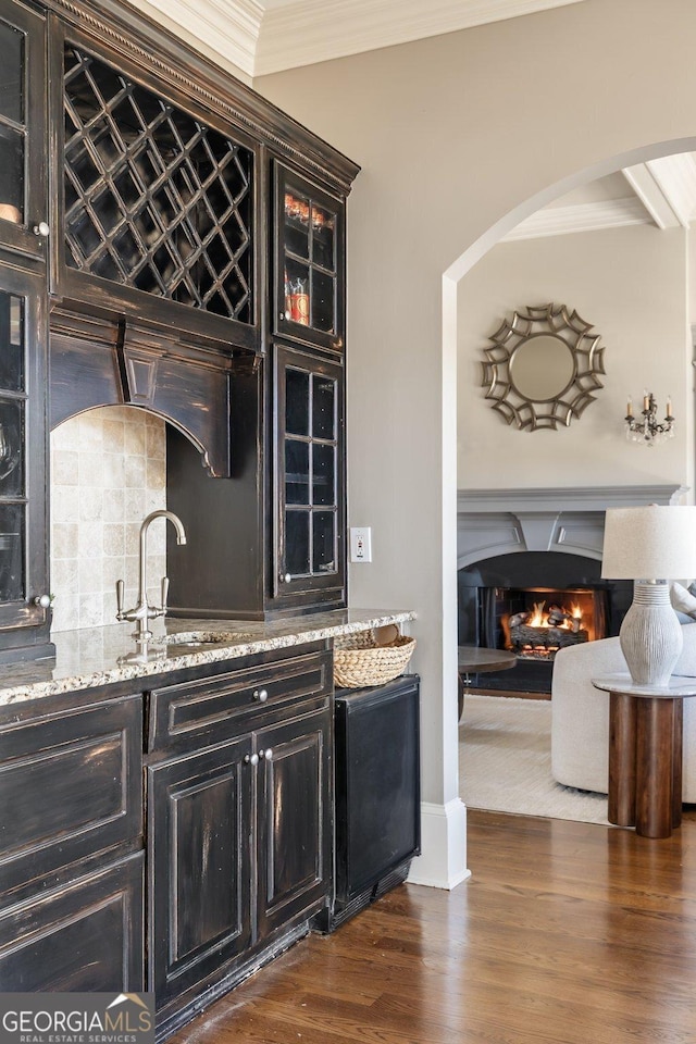 bar featuring sink, dark wood-type flooring, crown molding, and light stone countertops