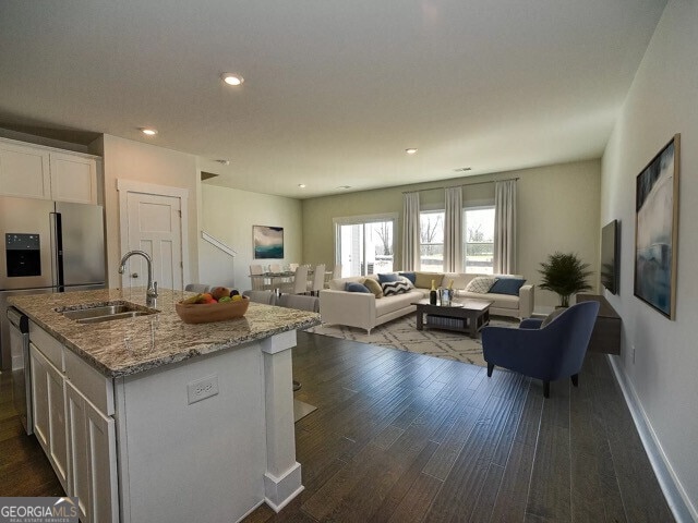 kitchen featuring an island with sink, sink, white cabinets, dark hardwood / wood-style flooring, and light stone countertops