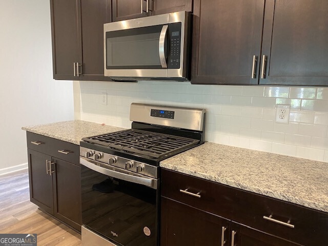 kitchen featuring appliances with stainless steel finishes, dark brown cabinets, light stone counters, tasteful backsplash, and light hardwood / wood-style floors