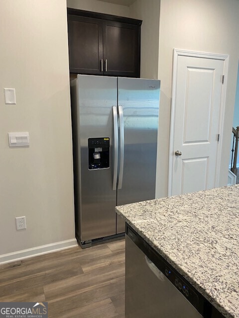 kitchen featuring stainless steel appliances, hardwood / wood-style flooring, dark brown cabinetry, and light stone counters