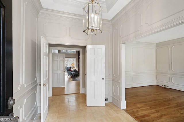 corridor with an inviting chandelier, ornamental molding, a decorative wall, and light wood finished floors