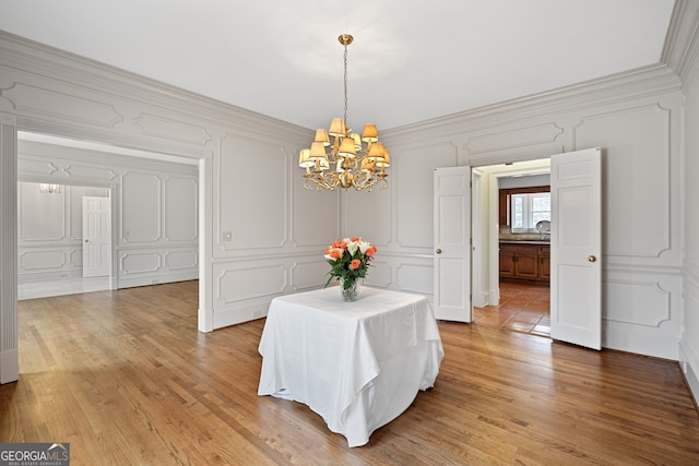 dining area featuring crown molding, wood finished floors, a notable chandelier, and a decorative wall