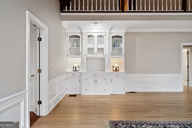 room details with built in shelves, a wainscoted wall, wood finished floors, visible vents, and ornamental molding