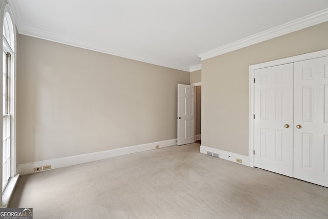 unfurnished bedroom with baseboards, visible vents, light colored carpet, ornamental molding, and a closet