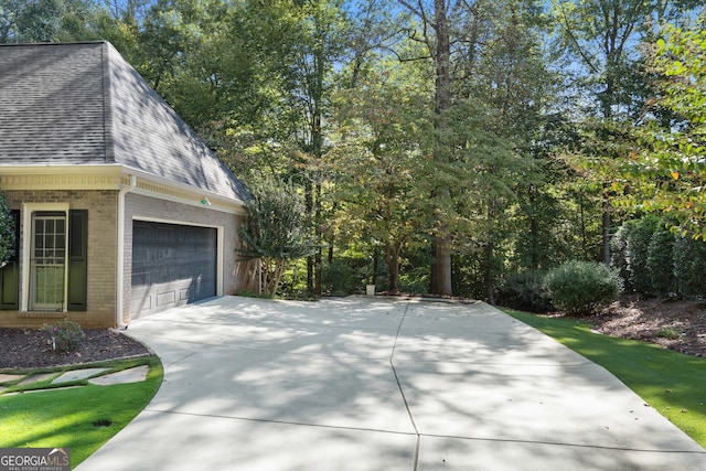 view of side of home with a garage, concrete driveway, brick siding, and a shingled roof