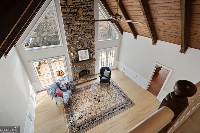 living room with wood ceiling, light wood-style flooring, a stone fireplace, high vaulted ceiling, and beam ceiling