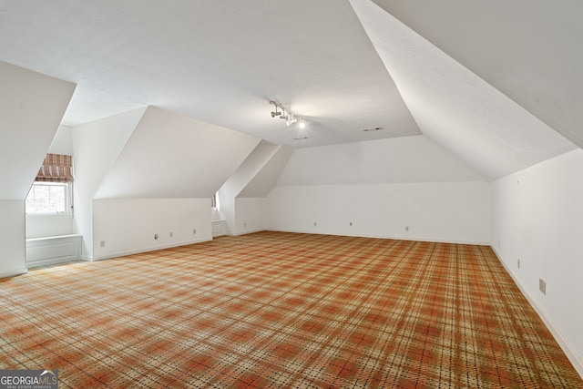 additional living space with vaulted ceiling, a textured ceiling, and baseboards