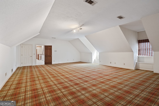 additional living space with a textured ceiling, vaulted ceiling, visible vents, and baseboards