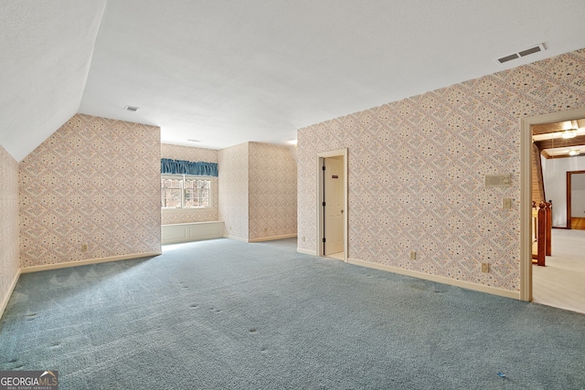 spare room featuring lofted ceiling, visible vents, carpet flooring, and wallpapered walls