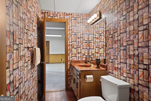 half bath with toilet, a wainscoted wall, a textured ceiling, and vanity