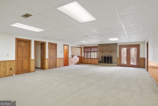 unfurnished living room featuring light carpet, wood walls, wainscoting, and visible vents